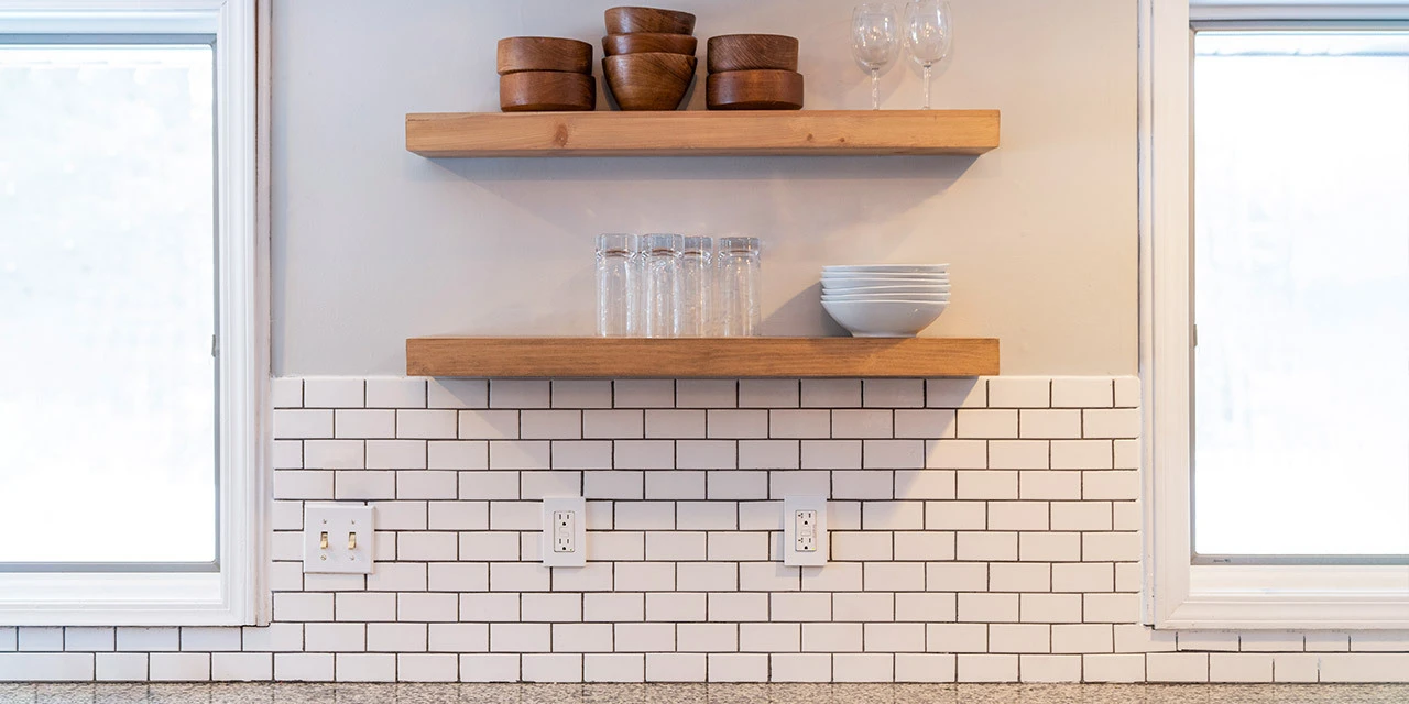 subway tile kitchen backsplash surrounded by two windows and shelves above it