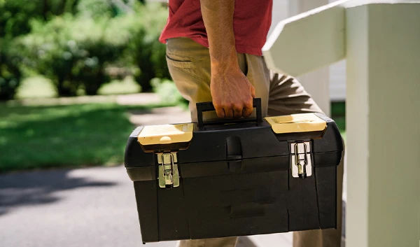 Close-up of handyman in red polo shirt and khaki pants carrying large black toolbox.